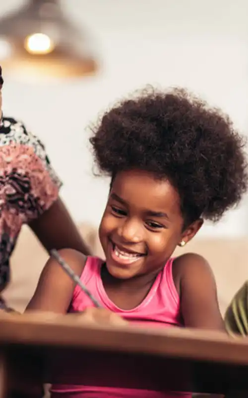 An African American family smiling at their child who is holding a pencil and smiling.