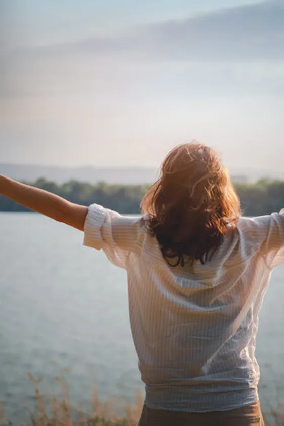 Woman with outstretched hands facing a lake